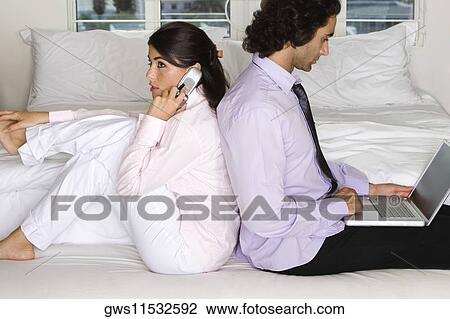 Stock Image - Side profile of a businessman and a businesswoman sitting back to back on the bed. Fotosearch