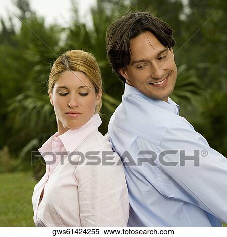 Stock Photography - Side profile of a businessman and a businesswoman sitting back to back in the park. Fotosearch