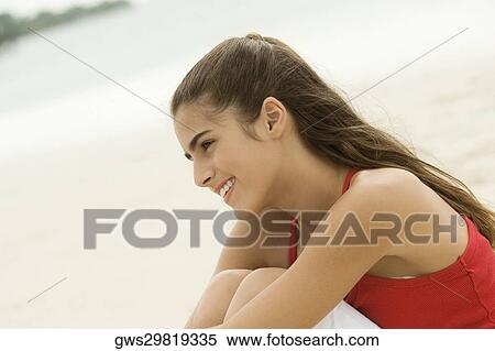 Stock Photography - Side profile of a girl sitting on the beach smiling. Fotosearch