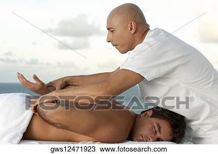 Stock Image - Side profile of a mature man giving a mid adult man a back massage. Fotosearch