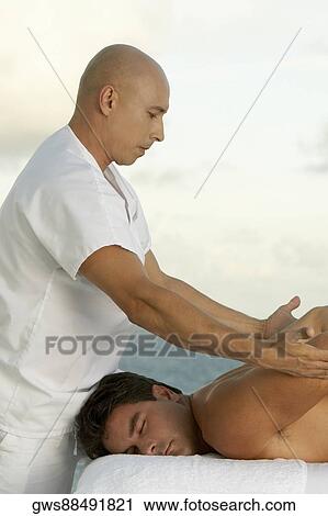 Side profile of a mature man giving a mid adult man a back massage View Large Photo Image Stock Image - Side profile of a mature man giving a mid adult man a back massage. Fotosearch