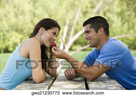 Stock Image - Side profile of a mid adult man feeding a young woman a strawberry. Fotosearch