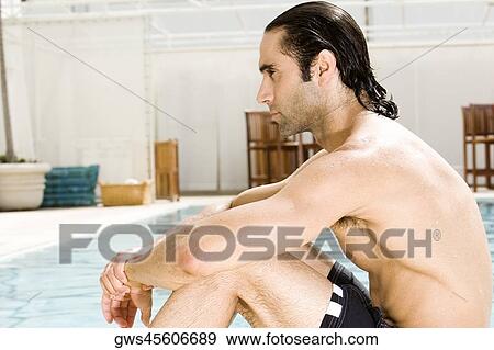 Stock Photo - Side profile of a mid adult man sitting at the poolside. Fotosearch