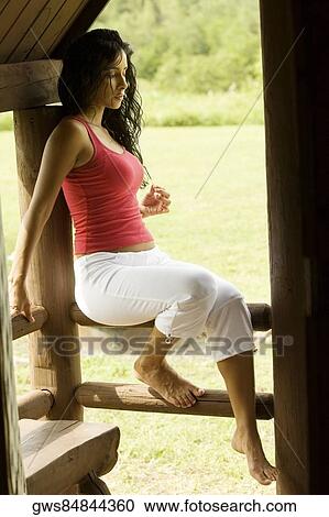 Stock Image - Side profile of a young woman leaning against a wooden column. Fotosearch