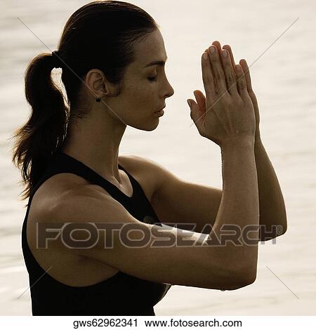 Stock Image - Side profile of a young woman meditating in a lake. Fotosearch