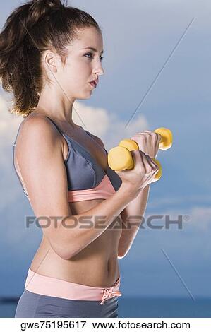 Side profile of a young woman exercising with dumbbells View Large Photo Image Stock Photo - Side profile of a young woman exercising with dumbbells. Fotosearch
