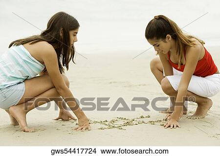 Side profile of two teenage girls drawing on sand on the beach View Large Photo Image Picture - Side profile of two teenage girls drawing on sand on the beach. Fotosearch