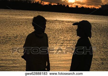 Stock Image - Silhouette of two boys standing on the beach. Fotosearch