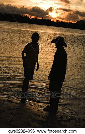 Stock Photograph - Silhouette of two boys standing on the beach. Fotosearch