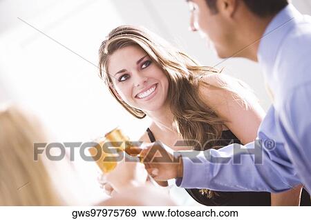 Stock Photo - Two young women and a mid adult man toasting. Fotosearch