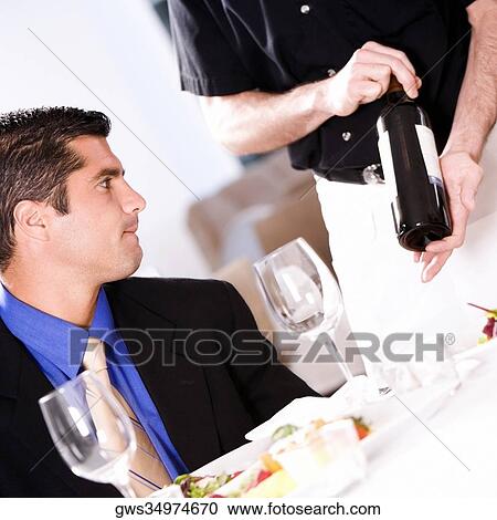 Stock Image - Waiter showing a wine bottle to a mid adult man. Fotosearch