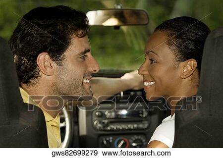 Stock Photo - Young woman and a mid adult man sitting in a car looking at each other. Fotosearch