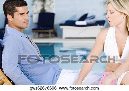 Young woman and a mid adult man sitting on a deck chair at the poolside View Large Photo Image Stock Photograph - Young woman and a mid adult man sitting on a deck chair at the poolside. Fotosearch