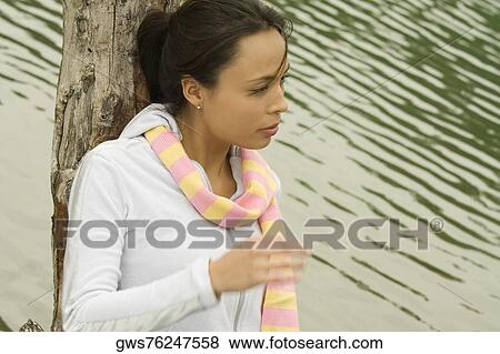 Young woman leaning against a tree trunk by the lake View Large Photo Image Stock Photo - Young woman leaning against a tree trunk by the lake. Fotosearch