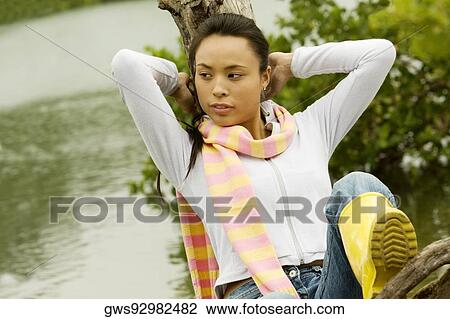 Stock Image - Young woman leaning against a tree stump. Fotosearch