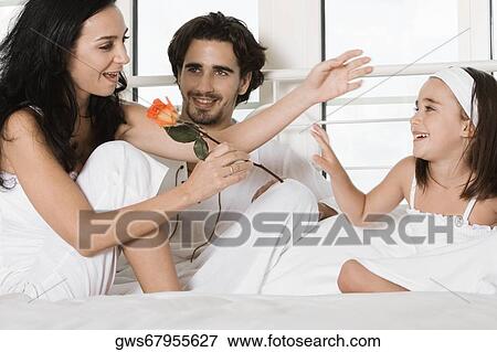 Young woman sitting on the bed holding a flower with a young man and her daughter View Large Photo Image Stock Photo - Young woman sitting on the bed holding a flower with a young man and her daughter. Fotosearch