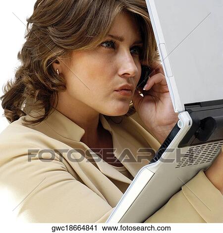 Stock Image - Close-up of a businesswoman holding a laptop while talking on a mobile phone. Fotosearch