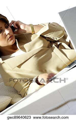 Stock Image - Close-up of a businesswoman talking on a mobile phone in front of a laptop. Fotosearch