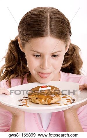 Close-up of a girl holding a donut in a plate licking her lips View Large Photo Image Stock Photo - Close-up of a girl holding a donut in a plate licking her lips. Fotosearch