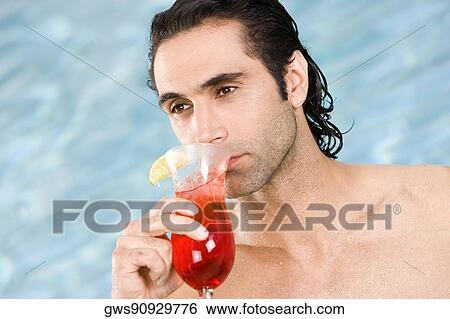 Stock Photograph - Close-up of a mid adult man drinking a cocktail near a swimming pool. Fotosearch