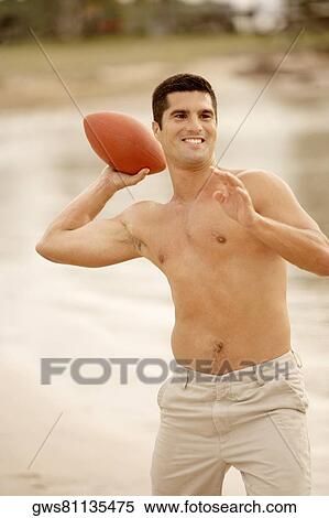 Stock Photography - Close-up of a mid adult man playing rugby on the beach. Fotosearch