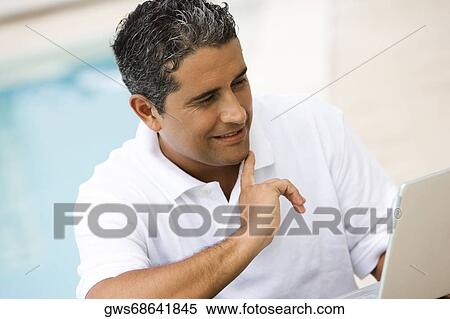 Close-up of a mid adult man using a laptop at the poolside View Large Photo Image Stock Photography - Close-up of a mid adult man using a laptop at the poolside. Fotosearch