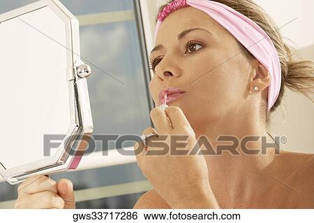 Close-up of a mid adult woman holding a mirror applying lipstick View Large Photo Image Stock Photograph - Close-up of a mid adult woman holding a mirror applying lipstick. Fotosearch