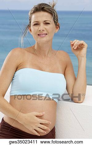 Close-up of a pregnant mid adult woman leaning against a wall with her hand on her abdomen View Large Photo Image Stock Image - Close-up of a pregnant mid adult woman leaning against a wall with her hand on her abdomen. Fotosearch