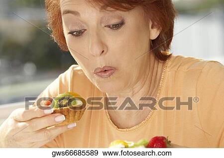 Stock Photo - Close-up of a senior woman eating a fruit tart. Fotosearch