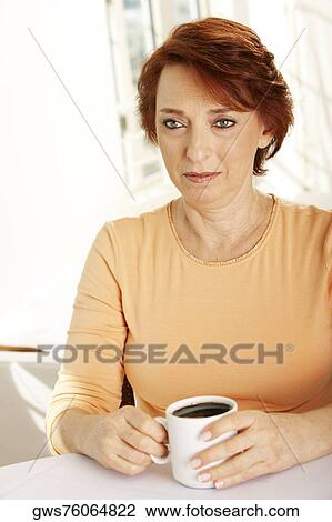 Stock Image - Close-up of a senior woman seated at a table with a cup of coffee. Fotosearch