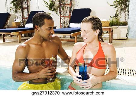 Stock Image - Close-up of a young couple holding glasses in a swimming pool. Fotosearch
