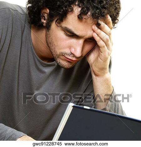 Stock Photography - Close-up of a young man in front of a laptop with his hand on his head. Fotosearch