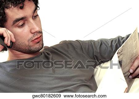 Close-up of a young man reading a newspaper and talking on a mobile phone View Large Photo Image Stock Photo - Close-up of a young man reading a newspaper and talking on a mobile phone. Fotosearch