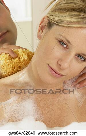 Stock Image - Close-up of a young man scrubbing a young woman's neck with a bath sponge. Fotosearch