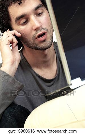 Close-up of a young man talking on a mobile phone in front of a laptop View Large Photo Image Stock Photograph - Close-up of a young man talking on a mobile phone in front of a laptop. Fotosearch