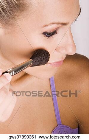 Stock Image - Close-up of a young woman applying blush with a brush. Fotosearch