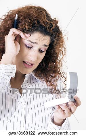Stock Image - Close-up of a young woman holding a calculator with her hand on her head. Fotosearch