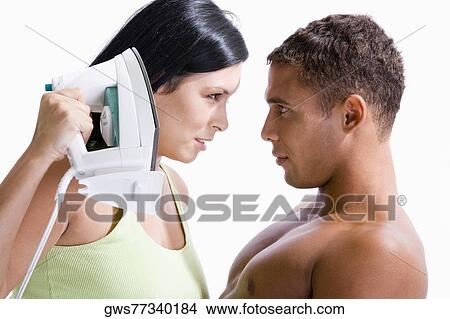Picture - Close-up of a young woman holding an iron in front of a young man. Fotosearch