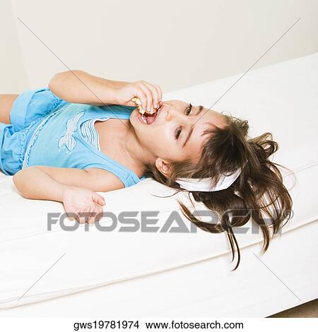 Picture - High angle view of a girl lying down and eating. Fotosearch