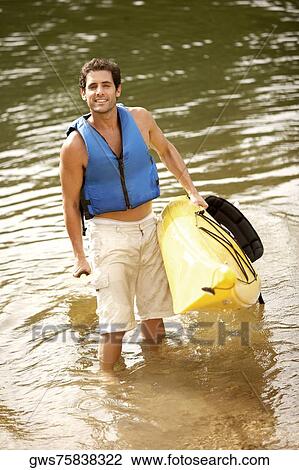 Stock Image - High angle view of a mid adult man holding a kayak and an oar. Fotosearch