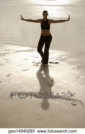 Stock Image - High angle view of a mid adult woman standing in the tree pose on the beach. Fotosearch