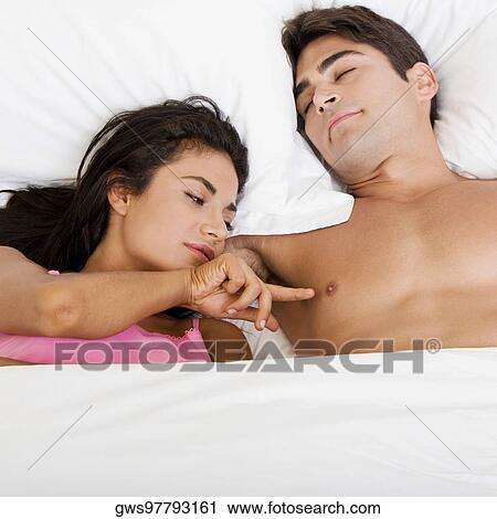 Stock Image - High angle view of a young couple lying on the bed. Fotosearch