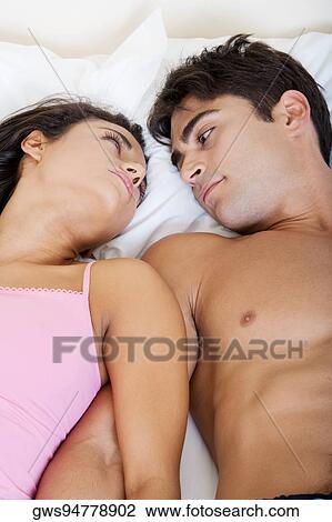 Stock Image - High angle view of a young couple looking at each other on a bed. Fotosearch
