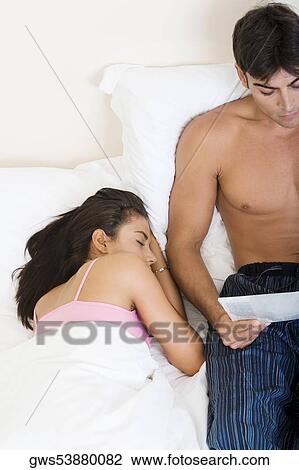 High angle view of a young man reading a paper with a young woman sleeping beside him View Large Photo Image Stock Image - High angle view of a young man reading a paper with a young woman sleeping beside him. Fotosearch