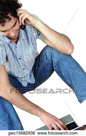 Stock Photo - High angle view of a young man talking on a mobile phone using a laptop. Fotosearch