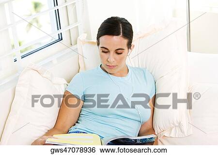 High angle view of a young woman wearing headphones and reading a magazine View Large Photo Image Stock Photograph - High angle view of a young woman wearing headphones and reading a magazine. Fotosearch