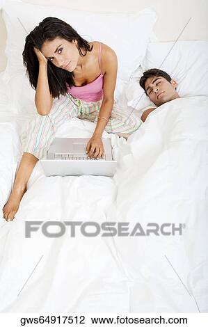 High angle view of a young woman using a laptop with a young man sleeping beside her View Large Photo Image Stock Image - High angle view of a young woman using a laptop with a young man sleeping beside her. Fotosearch