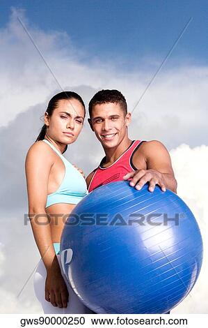 Stock Image - Low angle view of a young couple with an exercise ball. Fotosearch