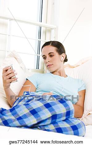 Picture - Low angle view of a young woman listening to an MP3 player. Fotosearch