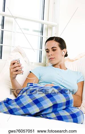 Stock Image - Low angle view of a young woman listening to an MP3 player. Fotosearch
